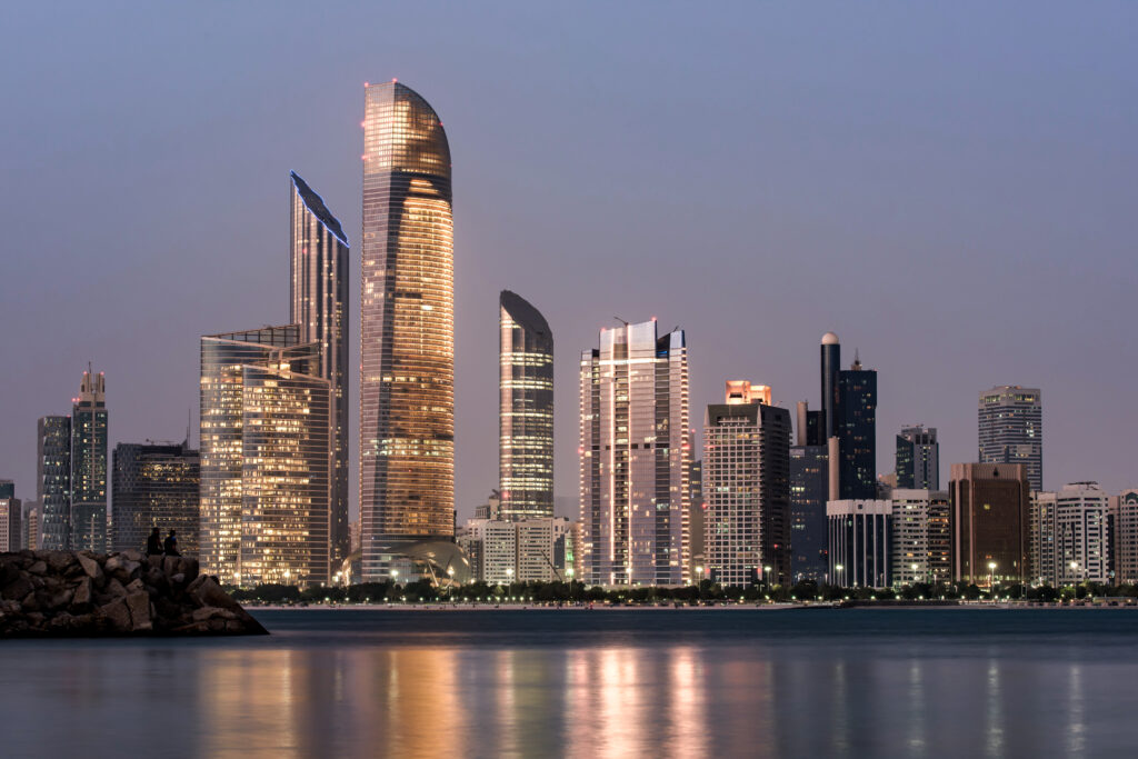 Abu Dhabi skyline at dusk reflected on calm waters, ideal for exploring the city with a car rental with driver service.