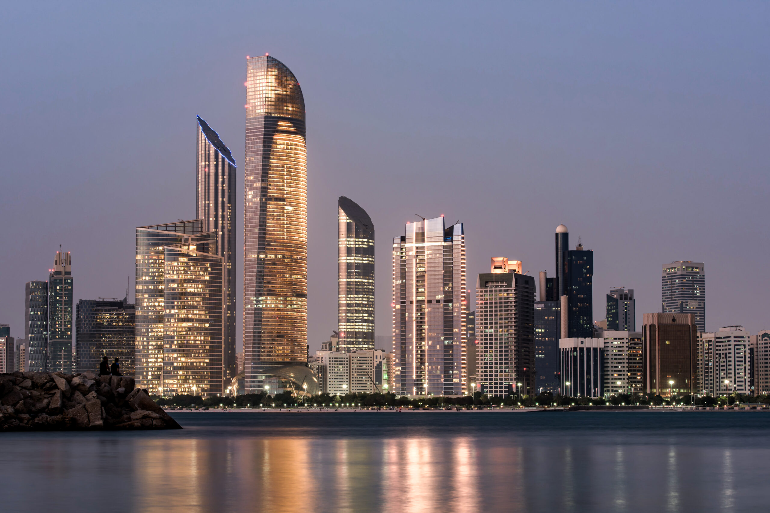 Abu Dhabi skyline at dusk reflected on calm waters, ideal for exploring the city with a car rental with driver service.